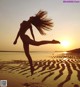 A woman jumping in the air on a beach at sunset.