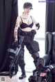 A woman in a black bra top and black pants holding a rifle.