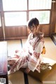 A woman in a kimono sitting on a pillow in a room.