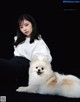 A woman sitting next to a white dog on a black background.