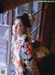 A woman in a kimono leaning against a window.