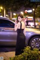 A woman in a black dress standing next to a car.