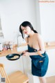 A woman in an apron holding a frying pan in a kitchen.