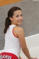 A woman in a white tank top and red shorts sitting on a bed.