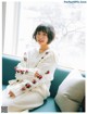 A woman sitting on a couch wearing a white sweater with red roses on it.